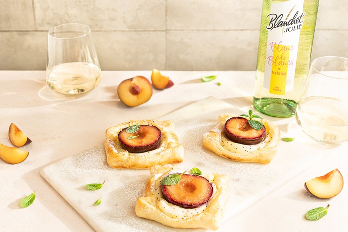 Drei köstliche Obsttörtchen mit Pflaumen und Minze auf einem Marmorbrett, umgeben von frischen Pflaumenstücken.