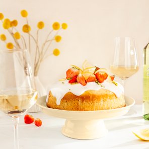 Ein köstlicher Kuchen mit einer weißen Glasur, garniert mit frischen Erdbeeren und Zitronenscheiben, steht auf einem eleganten Teller.