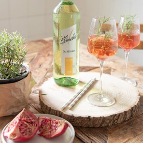 Zwei Gläser mit einem erfrischenden Getränk, garniert mit Rosmarin, stehen auf einem rustikalen Holztisch.