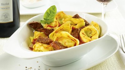 Ein elegantes Gericht mit gefüllten Teigtaschen, zartem Fleisch und frischem Basilikum, serviert in einer weißen Schüssel.