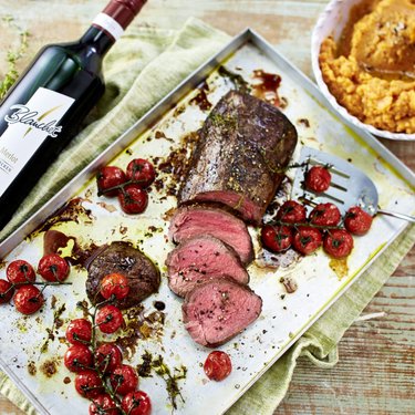 Ein saftiges Stück Rinderfilet, perfekt gebraten, liegt auf einem Blech, umgeben von gerösteten Kirschtomaten und Kräutern.
