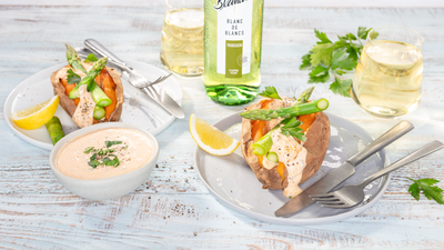 Ein Teller mit einer Süßkartoffel, belegt mit Spargel und Frischkäse, daneben ein Dip und ein Glas Weißwein.