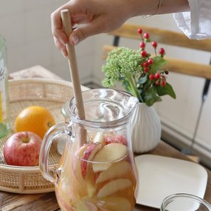Eine Hand rührt mit einem Holzlöffel in einem Krug, der mit Apfelscheiben und einer fruchtigen Mischung gefüllt ist.