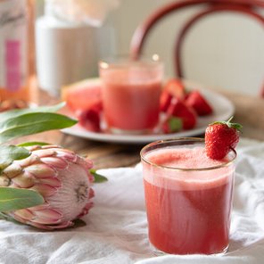 Ein Glas mit frischem Erdbeersaft, garniert mit einer Erdbeere, steht auf einem Tisch neben einer Platte mit frischen Früchten.